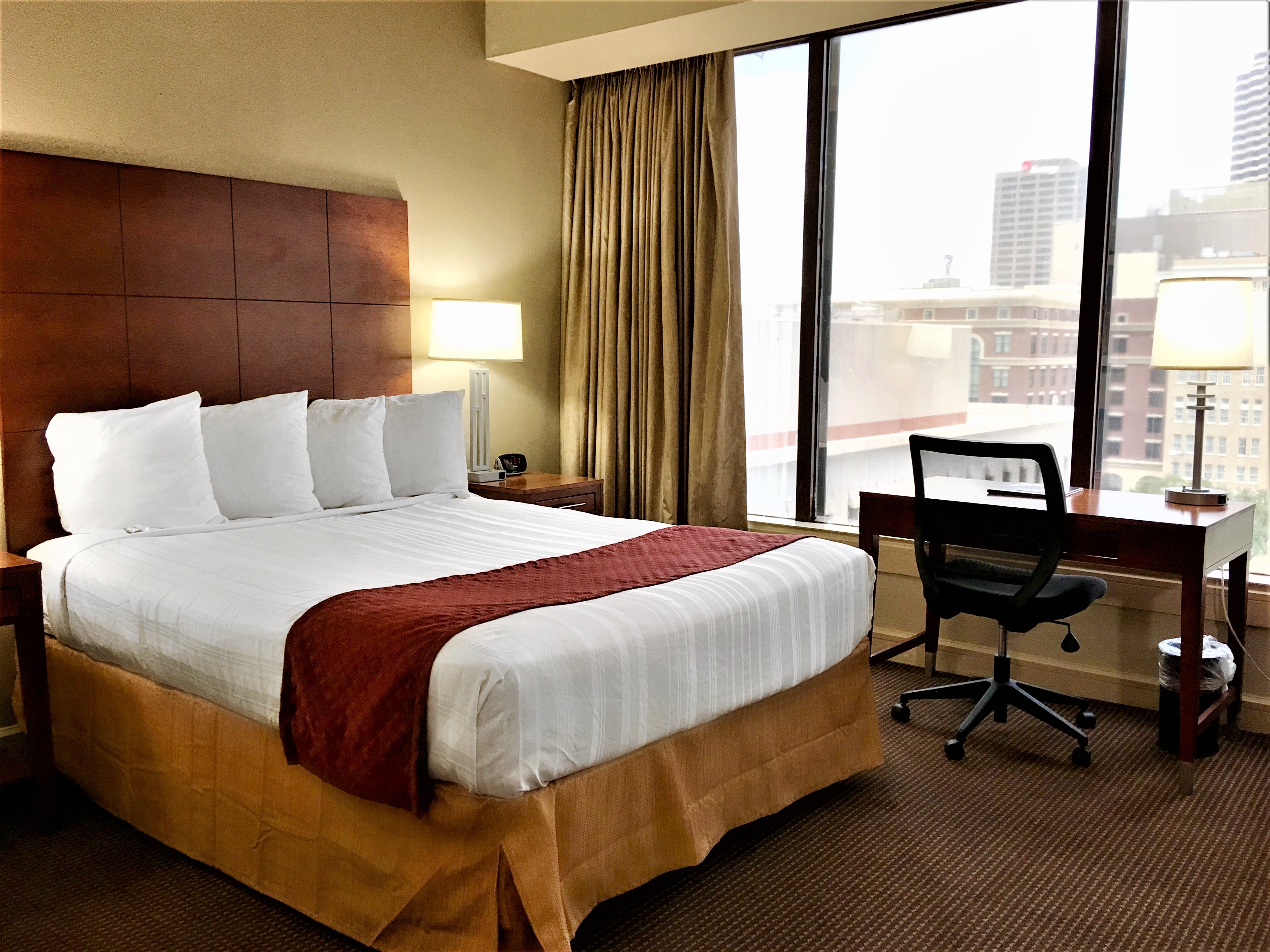 Blake Hotel New Orleans guest room with a neatly made bed, city view through large windows, and work desk.